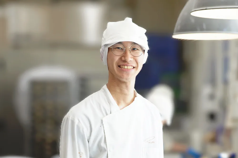 キッチンで笑顔を向ける男性の先輩パン職人のバストアップ写真